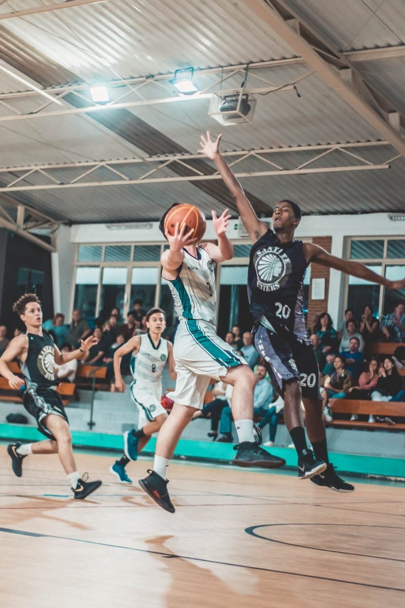 Een basketballer gaat naar de korf terwijl een tegenstander probeert te blokkeren